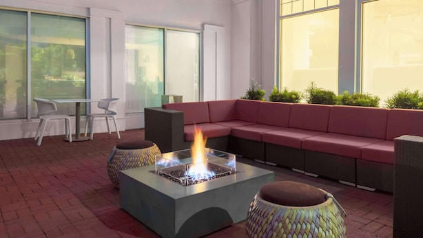 A modern outdoor seating area with a fire feature, wicker furniture, and large windows.