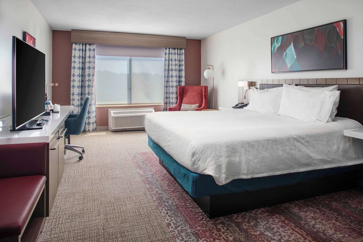 A hotel room with a large bed, a desk with a TV, a chair, and a window with curtains.