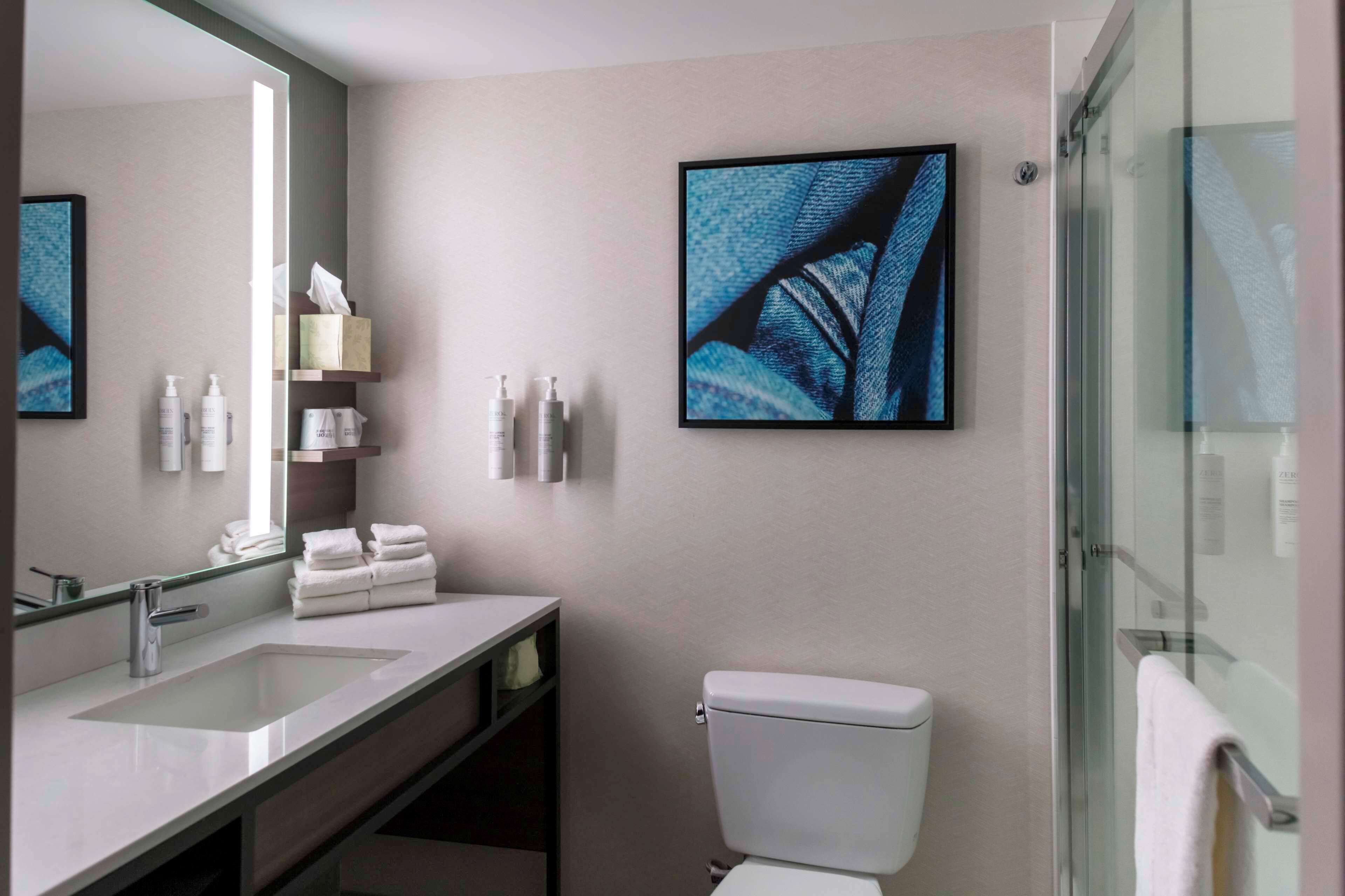 A modern bathroom with a large mirror, a sink, a toilet, and a glass shower enclosure.