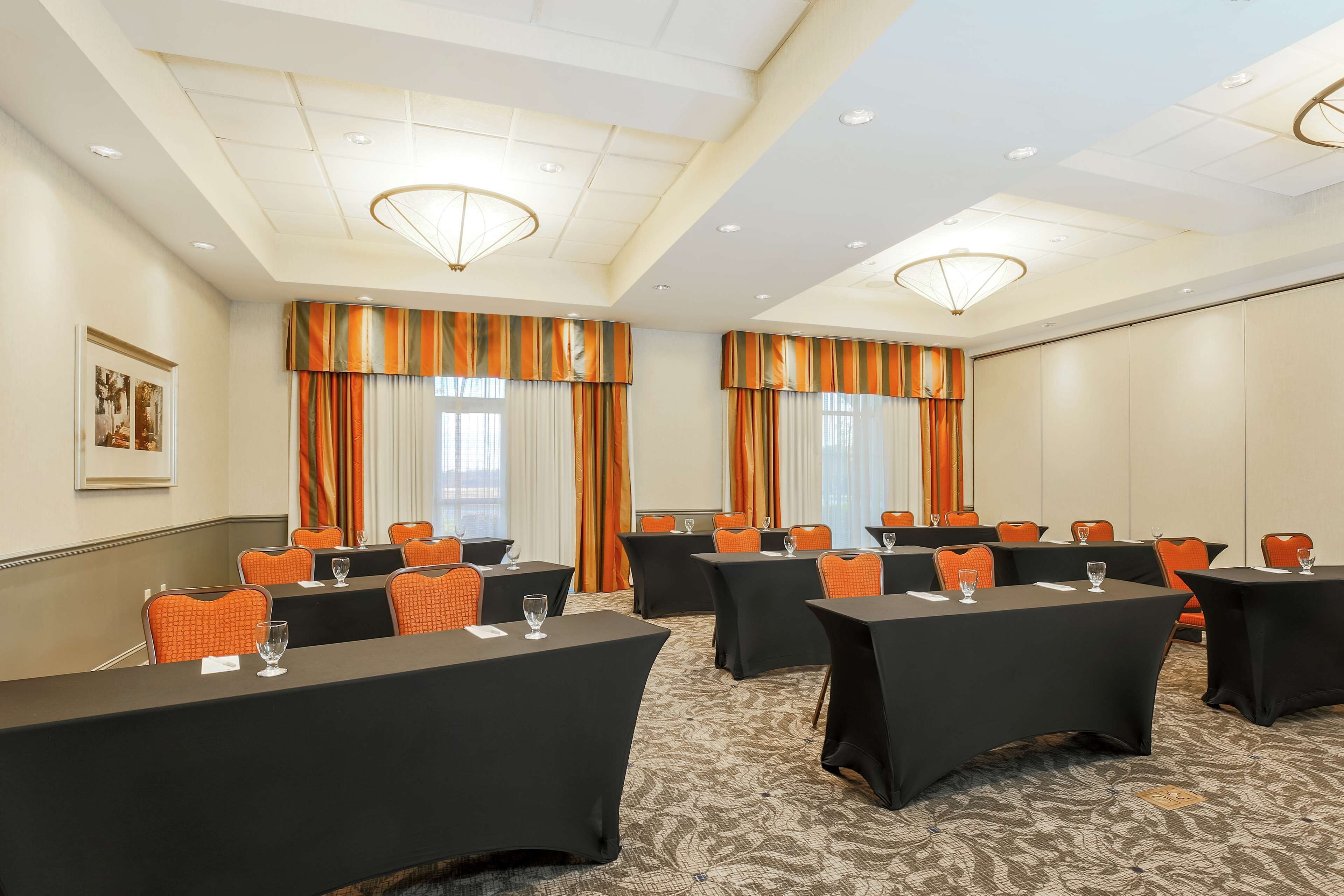 Une salle de conférence équipée de tables et de chaises, de grandes fenêtres avec des rideaux et d’un sol recouvert de moquette.