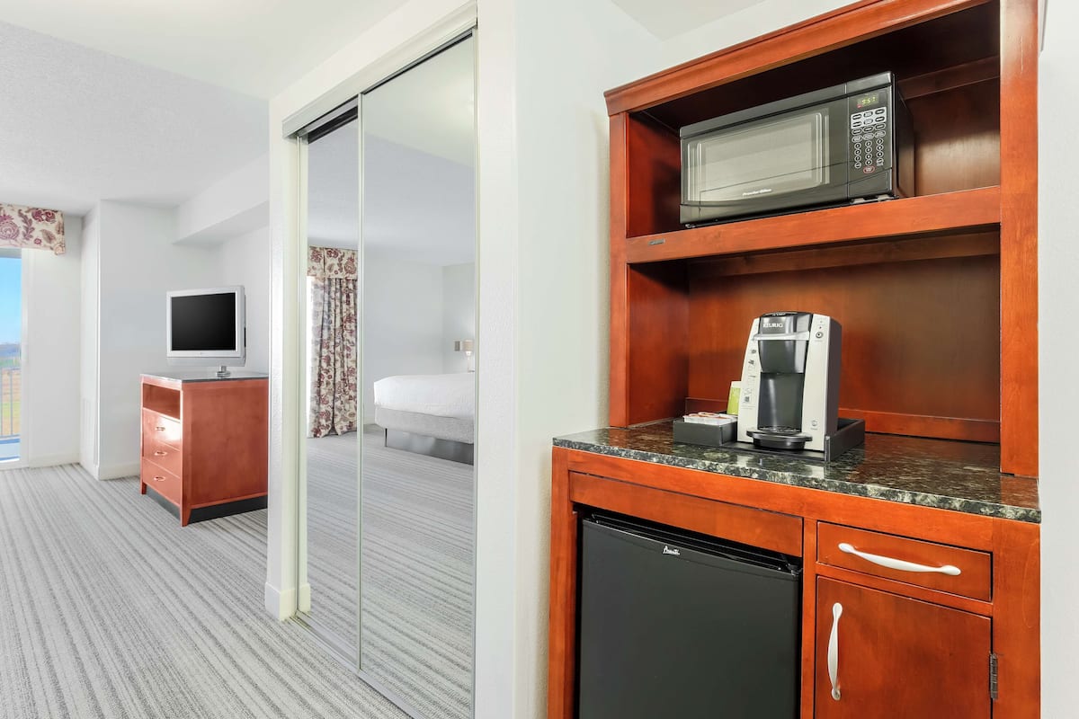 A hotel room with a kitchenette, a bed, a TV, and a sliding door leading to another room.