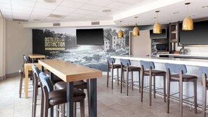 A modern bar area with a long counter, multiple stools, and a large mural depicting a river scene.