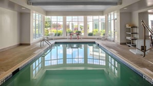 An indoor swimming pool with clear glass walls, a red table, and chairs near the windows.