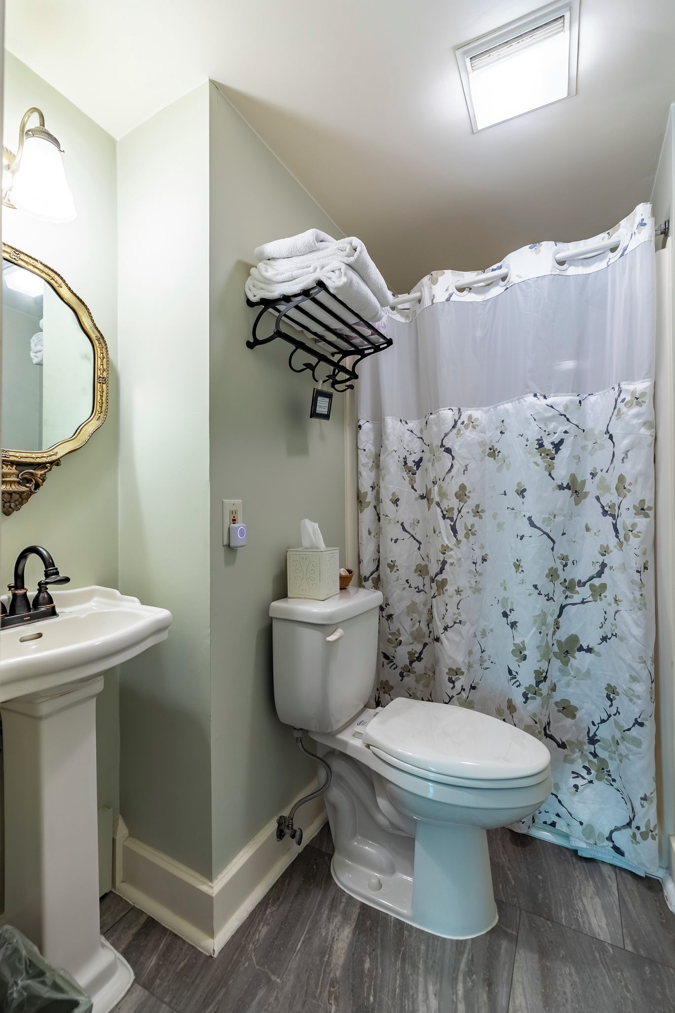 Une salle de bain avec des toilettes blanches, un lavabo, un miroir et un rideau de douche à motifs floraux.