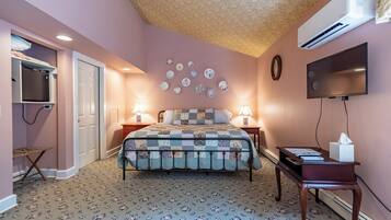 A bedroom with a bed, bedside lamps, a flat-screen TV, a wall-mounted air conditioner, and a decorative plate collection.