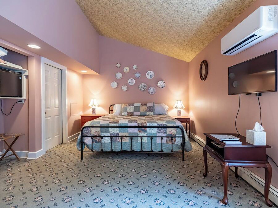 A bedroom with a bed, bedside lamps, a flat-screen TV, a wall-mounted air conditioner, and a decorative plate collection.