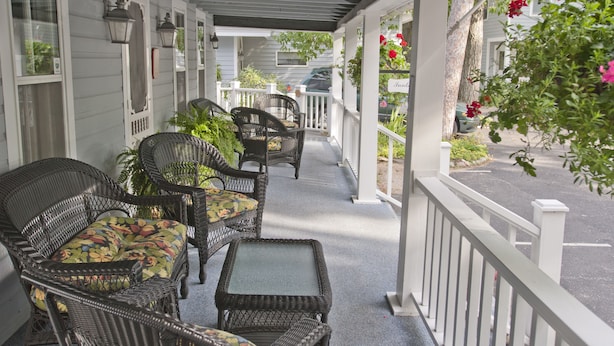 A covered porch with wicker furniture and potted plants. - The Sylvan Inn (Glen Arbor)