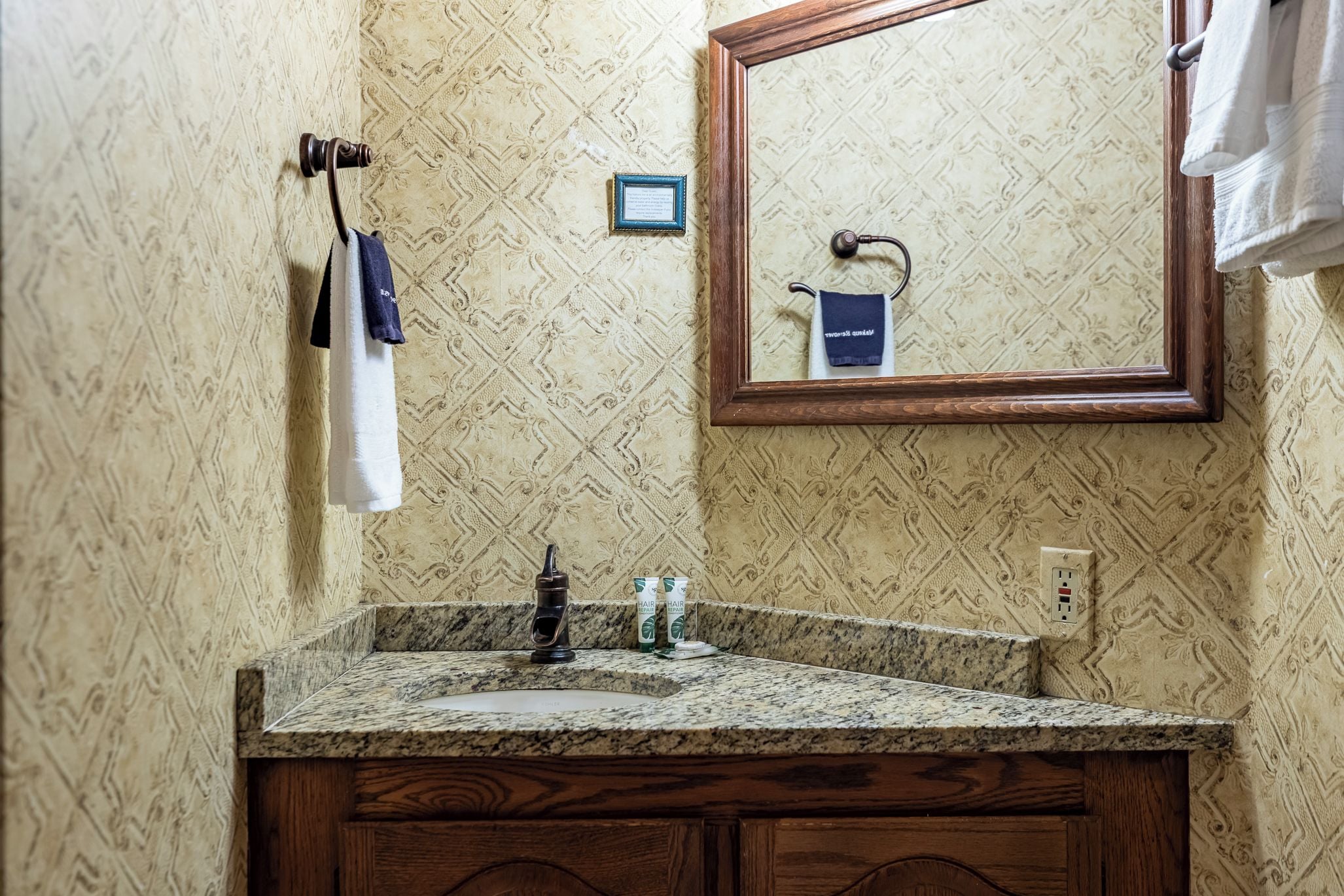 A bathroom with a wooden vanity, a sink, a mirror, and towels hanging on a rack.