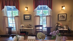 A cozy room with two windows, a table with a vase of flowers, and a chair. - The Sylvan Inn (Glen Arbor)