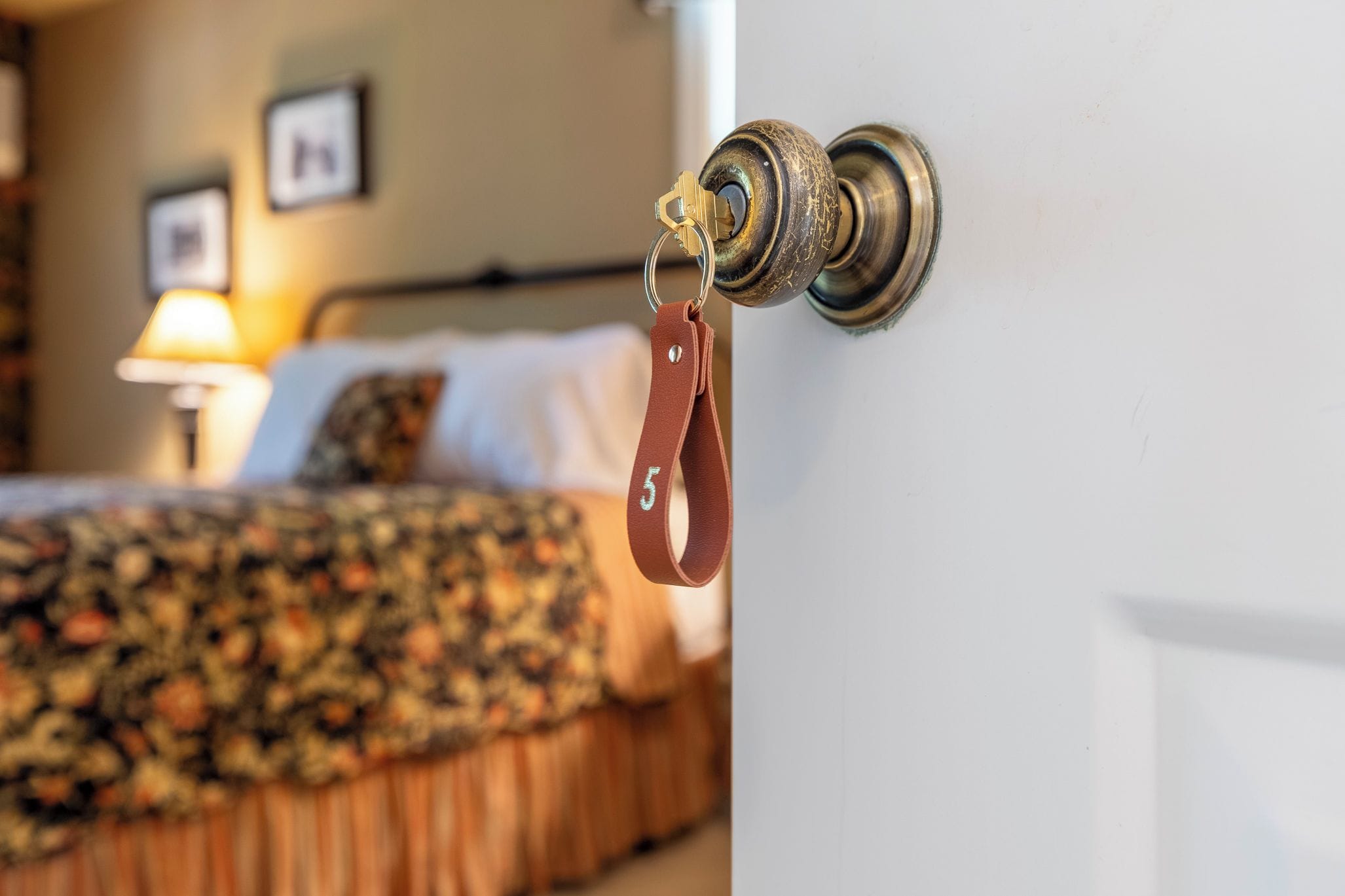 Eine Hotelzimmertür mit Schlüsselanhänger und ein Bett mit floralem Überwurf.