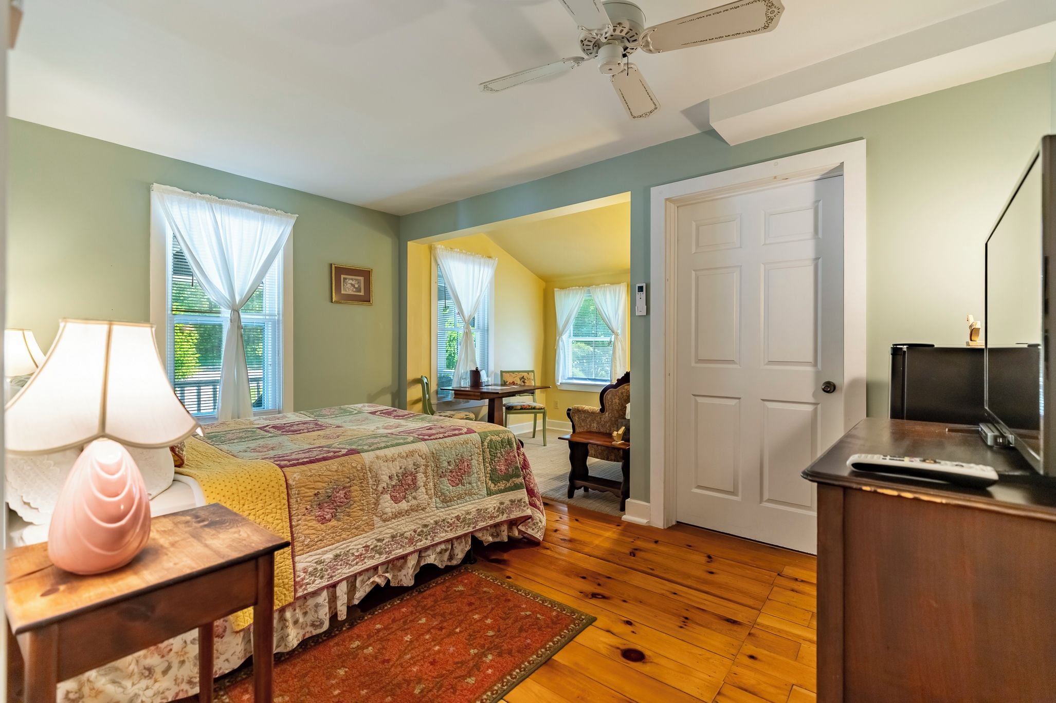 A bedroom with a bed, a desk, a chair, a television, and a door.