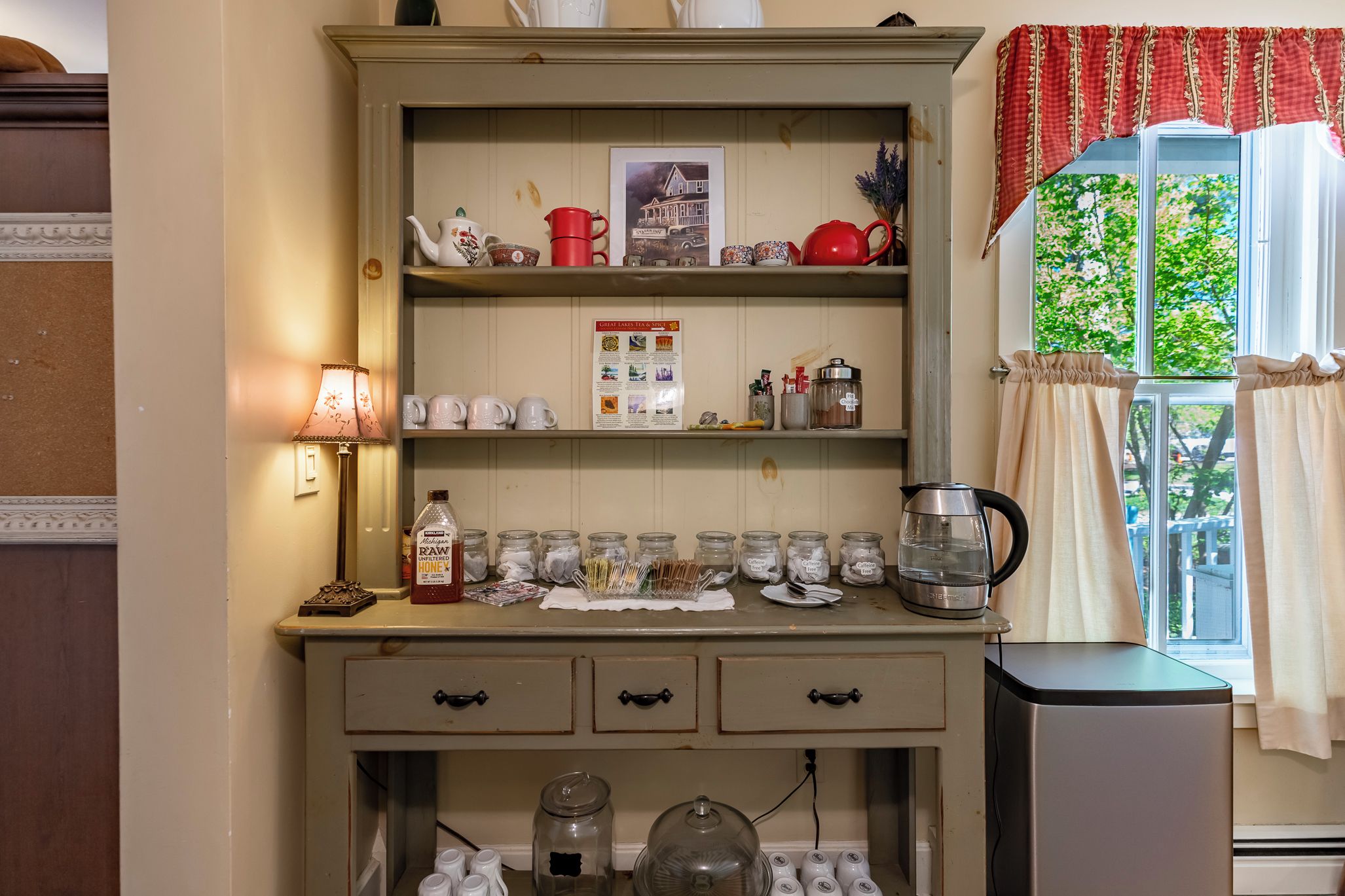 A kitchen with a wooden cabinet, a kettle, and various jars on the counter.