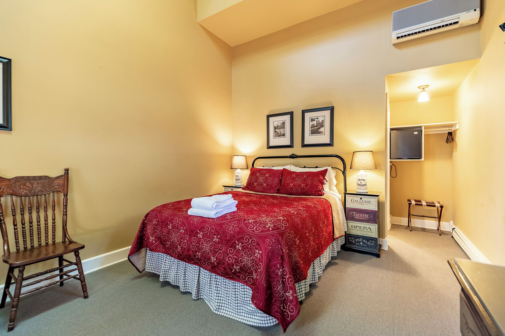 Un dormitorio con cama, una silla, una mesita de noche, una lámpara y aire acondicionado instalado en la pared.