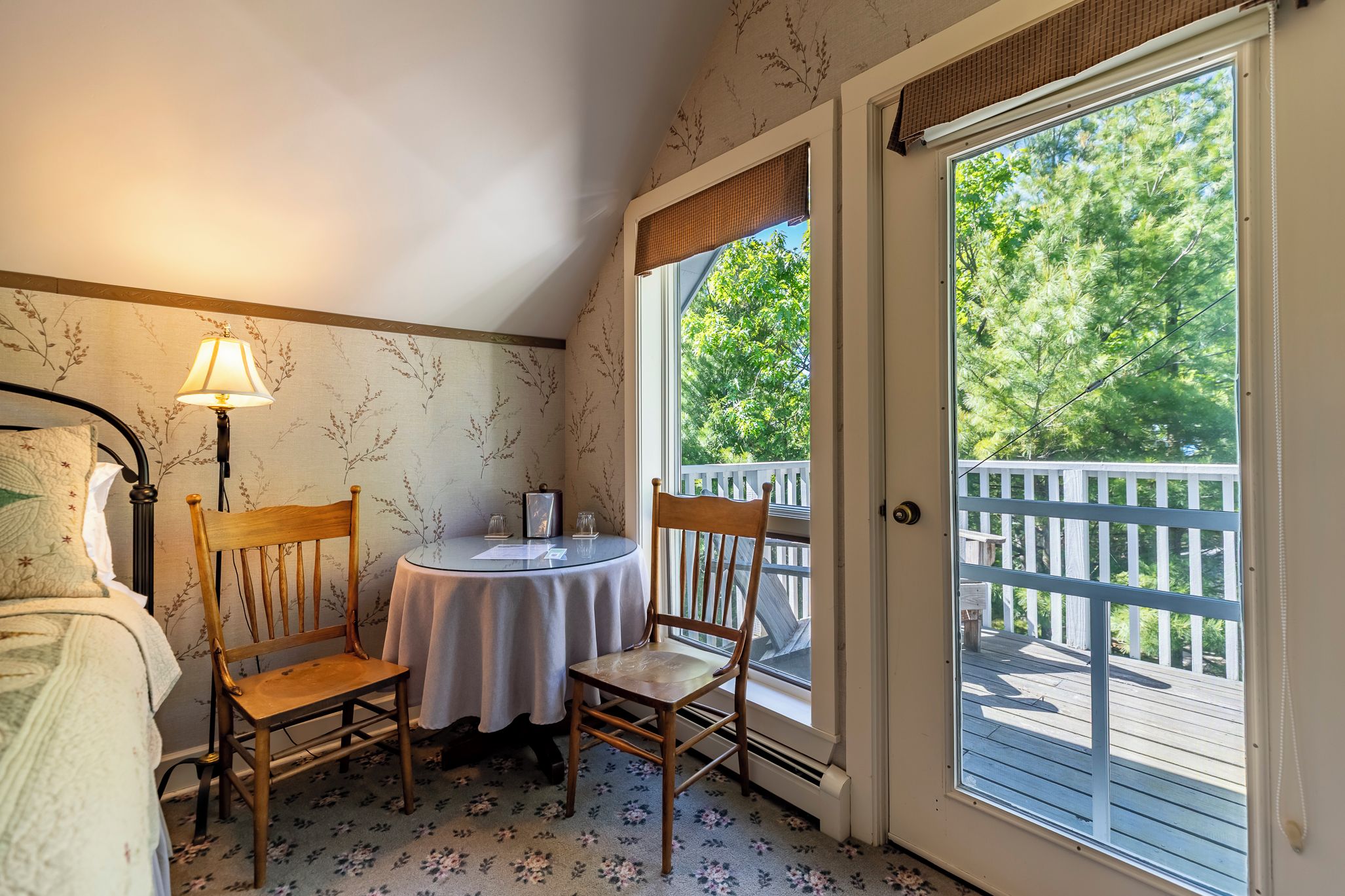 Una habitación con cama, una mesa con sillas, una lámpara y vista a una terraza por una puerta.