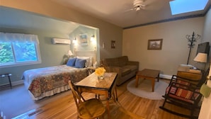 A cozy room with a bed, a sofa, a dining table with chairs, a small table with a lamp, and a rocking chair. - The Sylvan Inn (Glen Arbor)