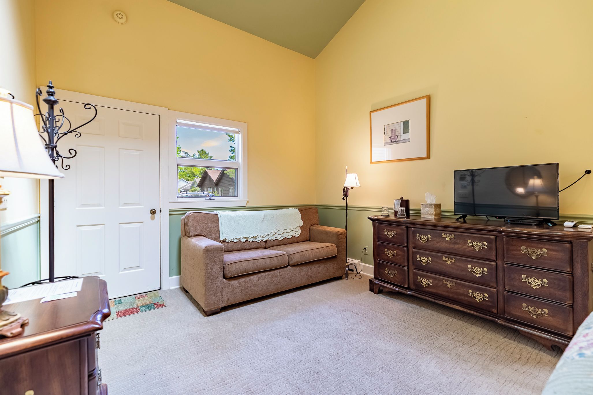A room with a beige sofa, a wooden dresser, a television, and a window with a view of houses.