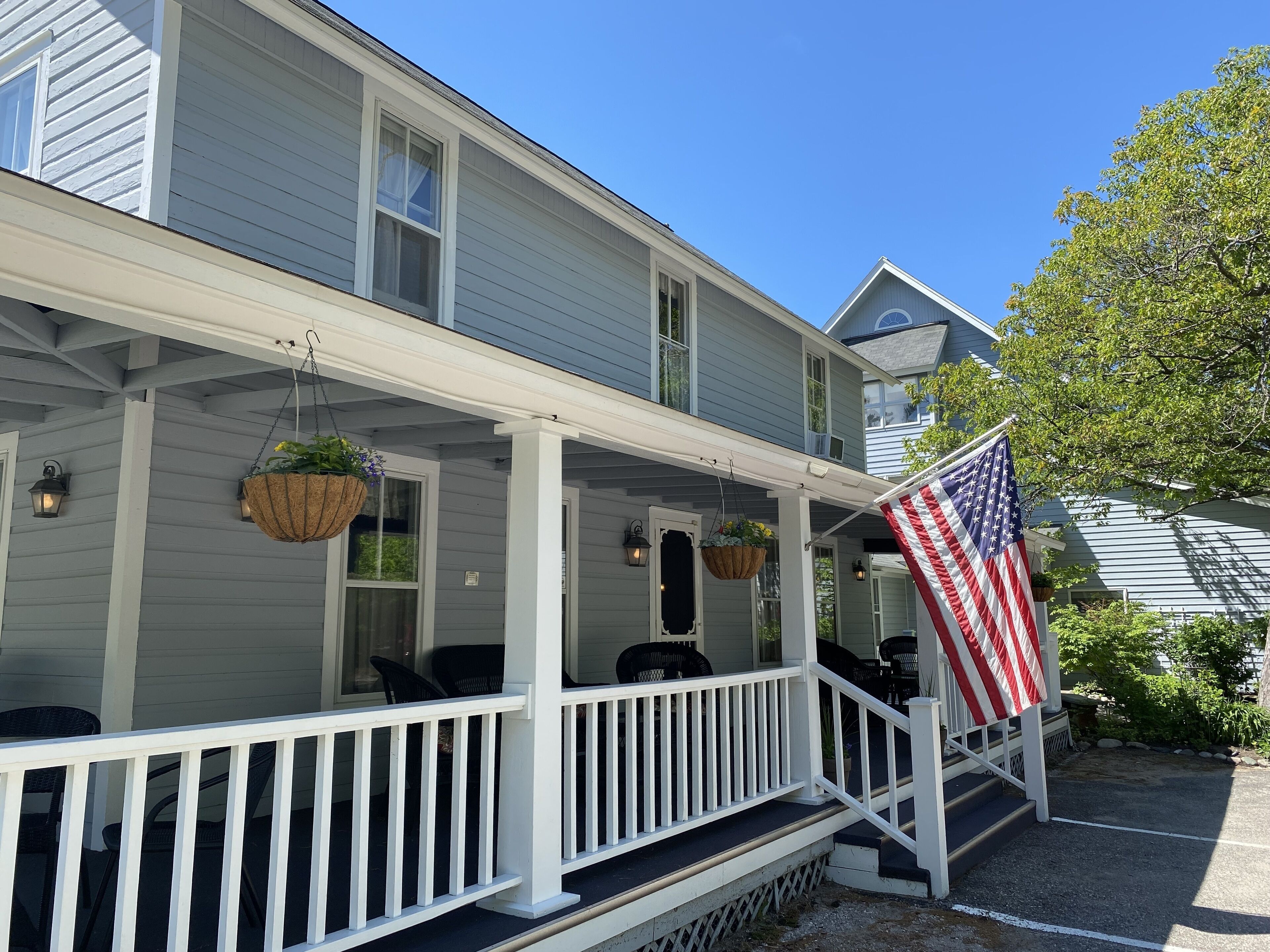 A two-story house with a porch, outdoor seating, and an American flag.