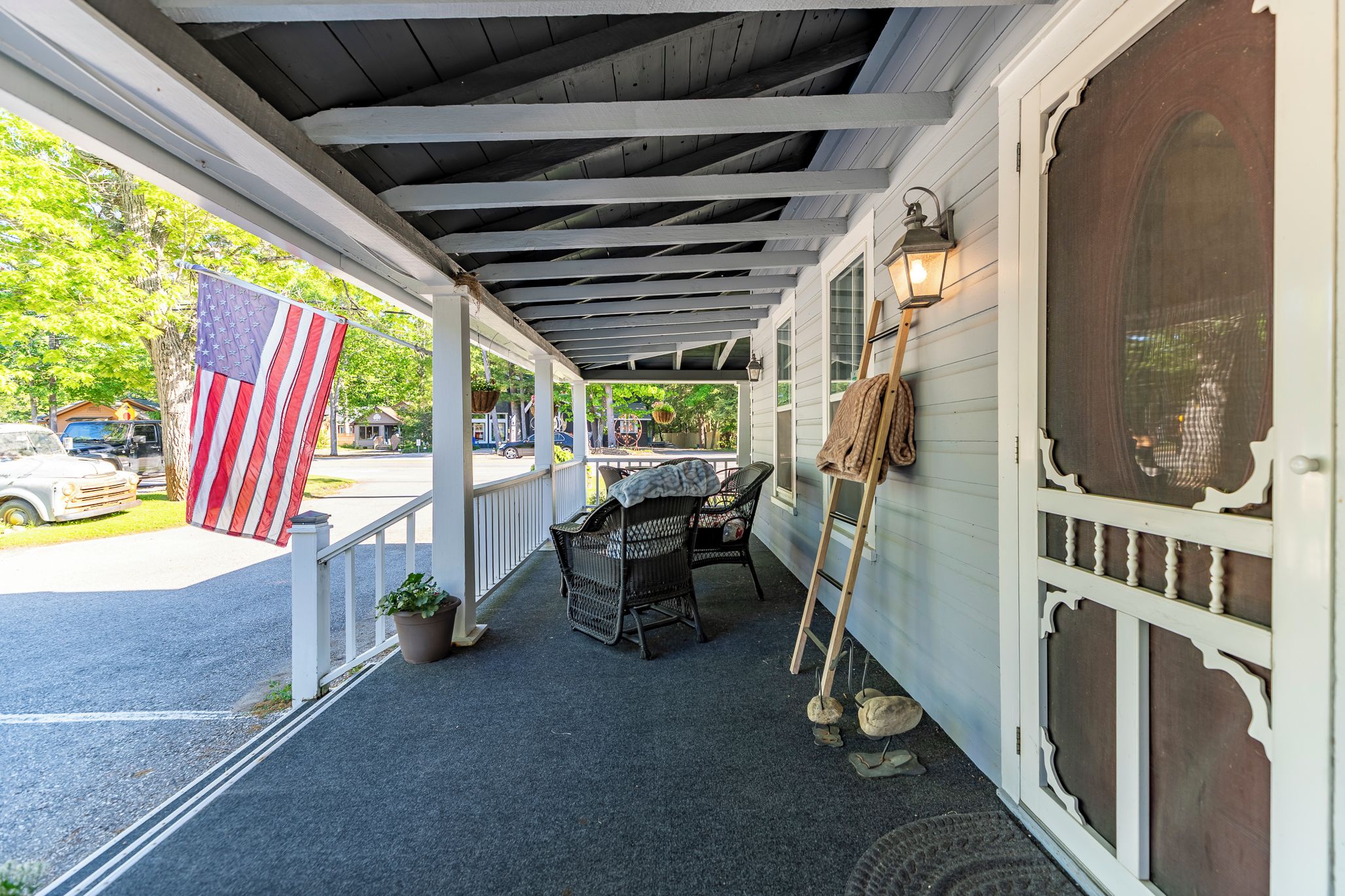 A covered porch with a table and chairs, a flag, and a ladder leaning against the wall.