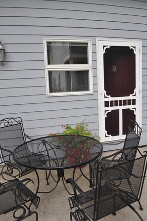 A patio with a round metal table and chairs, a window, and a door with a number.