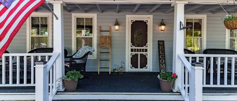 A porch with a welcome sign, steps, a flag, and potted plants.