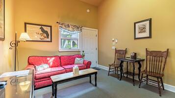A living room with a red sofa, a wooden coffee table, two wooden chairs, a white door, and framed pictures on the walls.