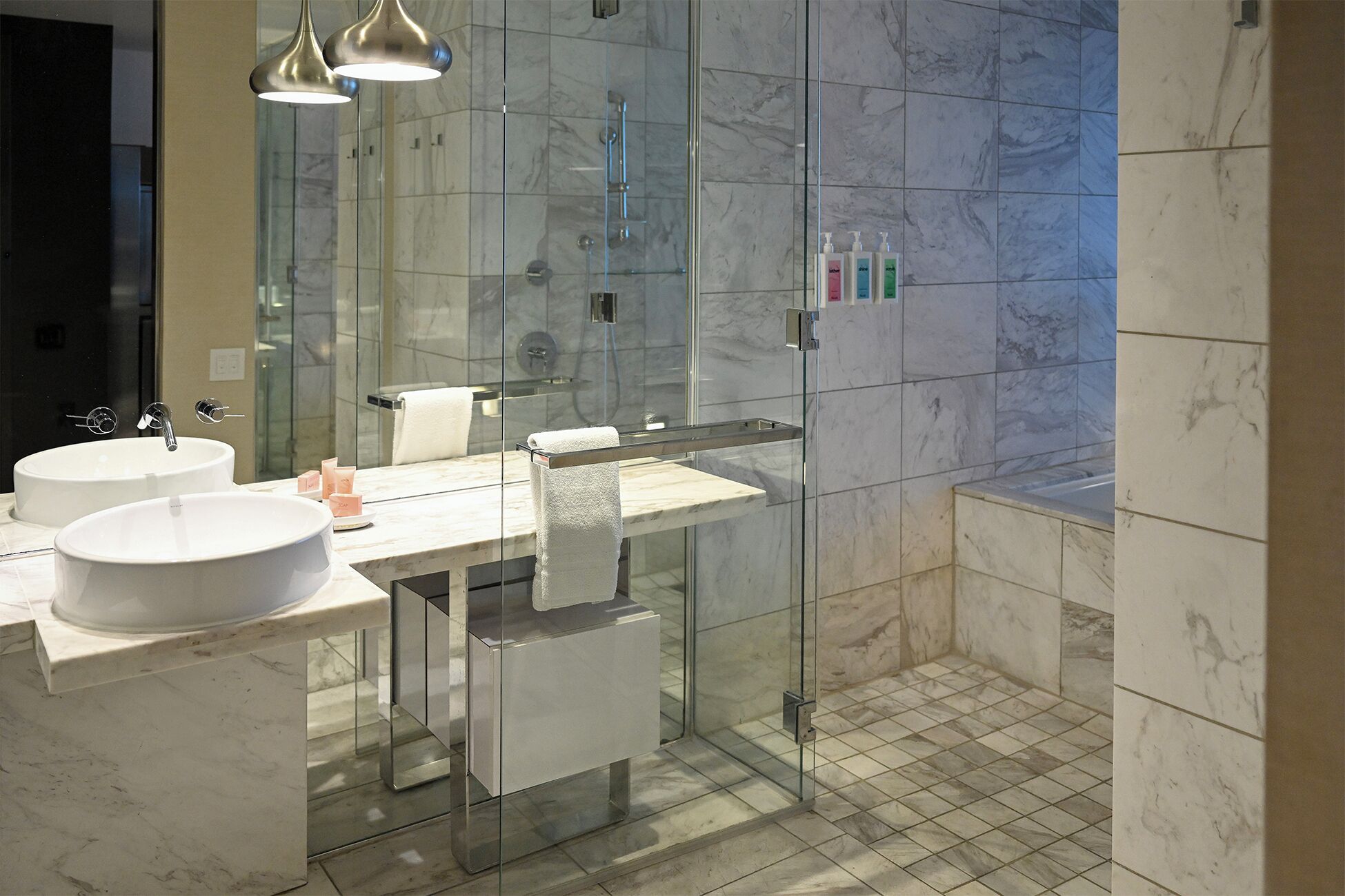 Un bagno moderno con due lavabi, cabina doccia in vetro e pavimento in marmo.