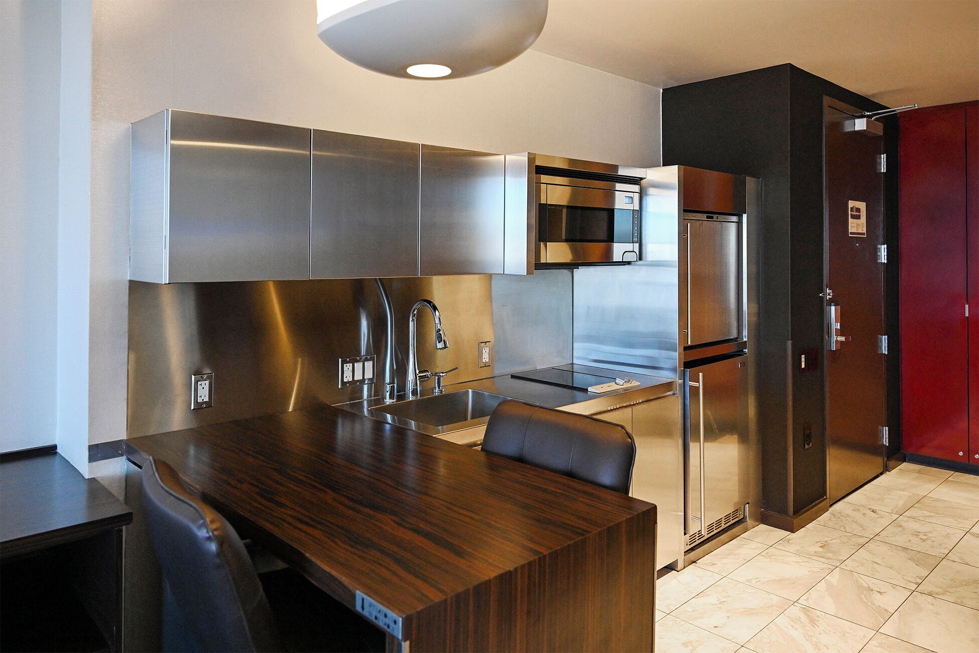 A modern kitchen with stainless steel appliances, a wooden dining table, and a red cabinet.