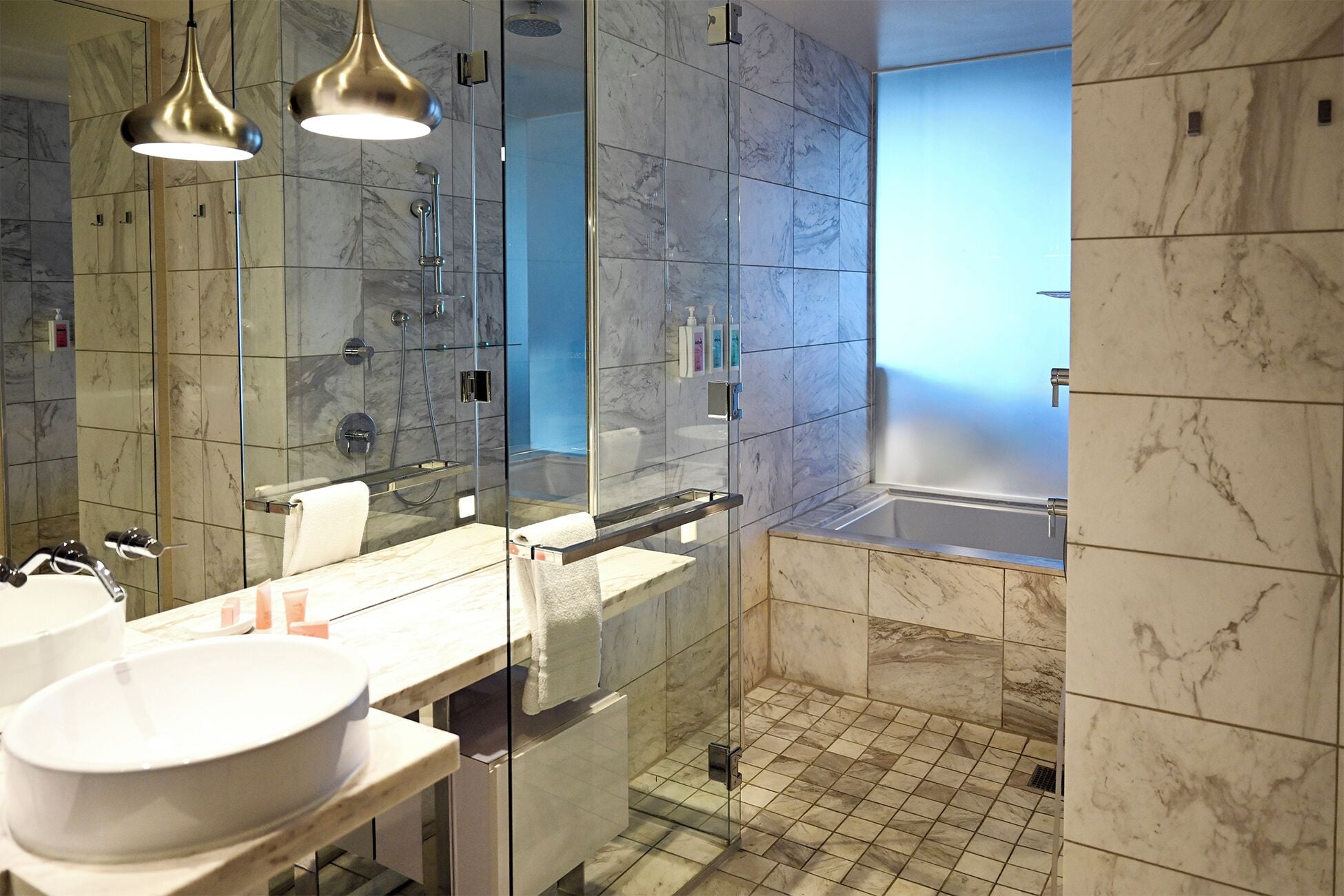 Een moderne badkamer met een douche in glazen cabine, een grote spiegel en een marmeren vloer.
