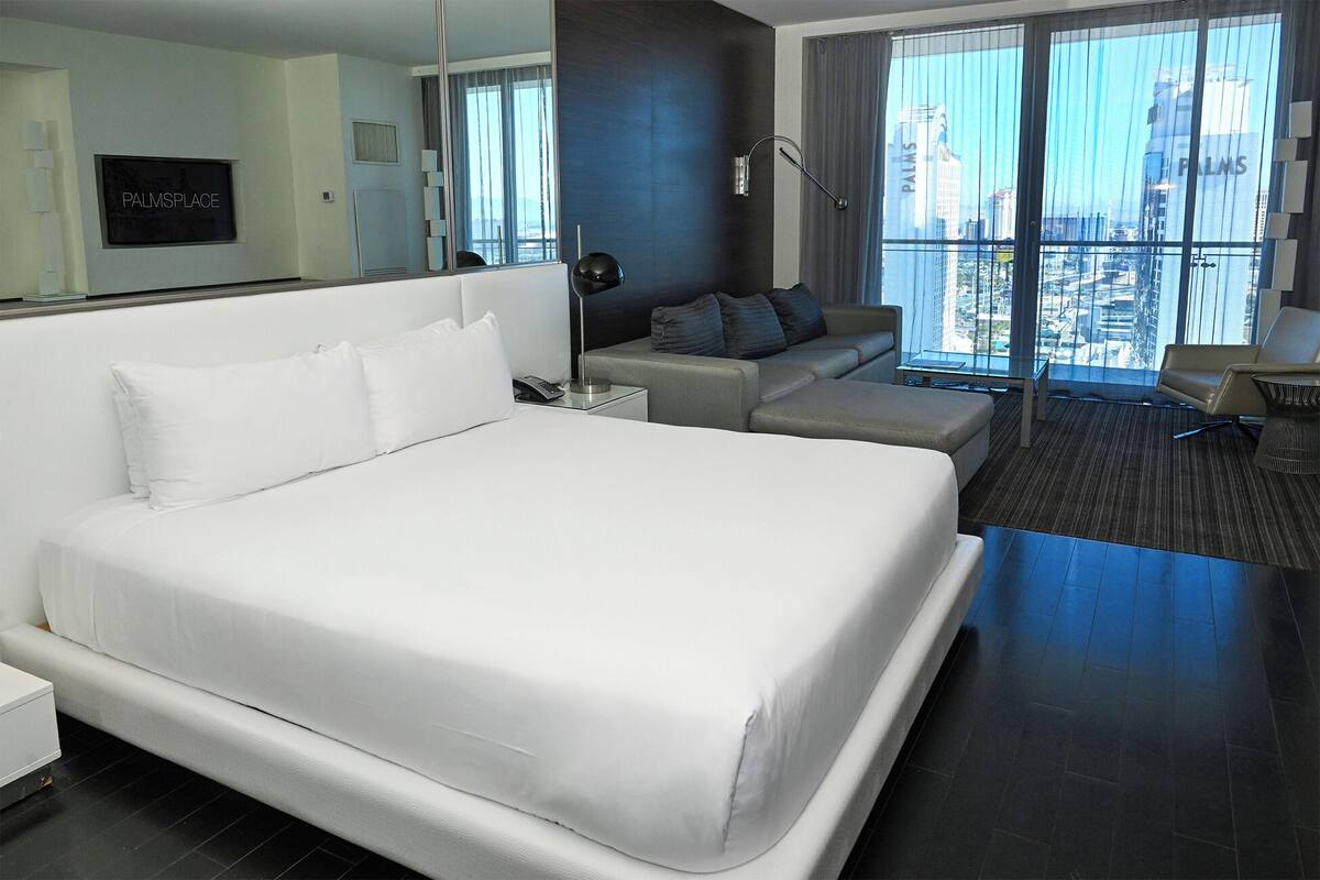 A hotel room with a large bed, a sofa, a desk, and a view of the city.