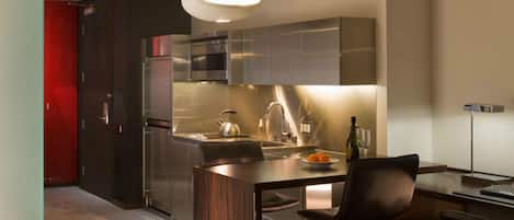 A modern kitchen with stainless steel appliances, a bar area with a high chair, and a pendant light.