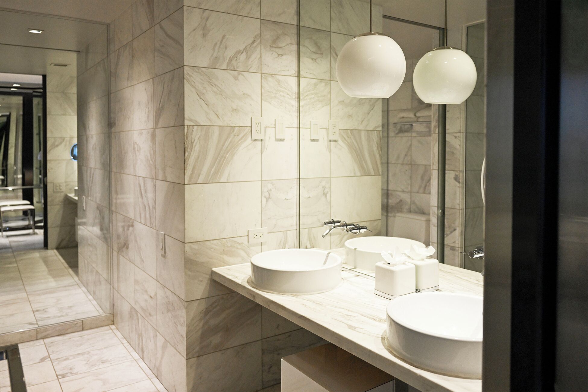 A modern bathroom with marble tiles, two sinks, and pendant lights.