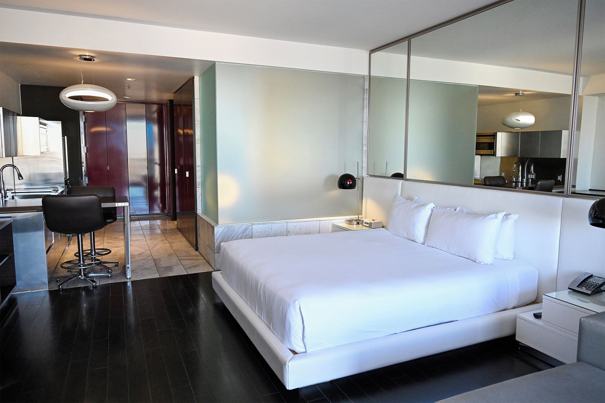 Een hotelkamer met een groot bed, een bureau, een stoel, een spiegel en een badkamer die door een open deur zichtbaar is.