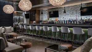 Un'area bar moderna con sgabelli alti, un bancone pieno di bottiglie e illuminazione a sospensione.