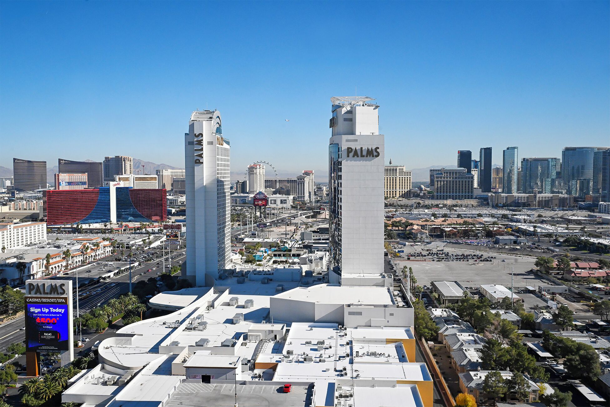 A high-rise building with 'PALMS' signage, surrounded by other skyscrapers and a parking area.