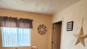 Una habitación con una mesa redonda de madera, dos sillas, un sofá, una decoración de pared con forma de estrella, un cuadro enmarcado y una ventana con persianas.