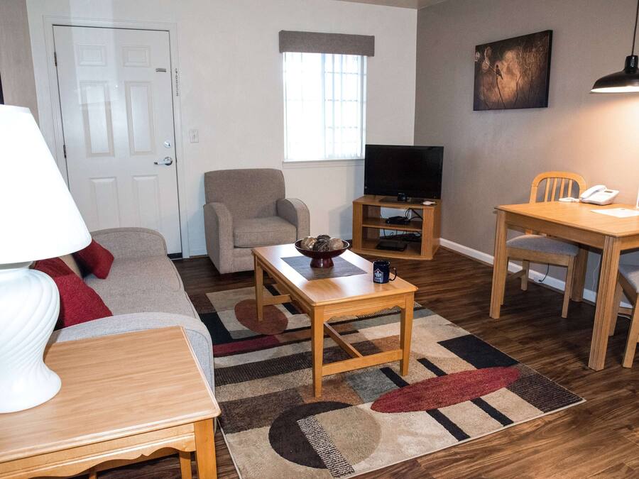 A living room with a sofa, a coffee table, a TV stand, a dining table with chairs, and a lamp.