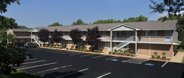 Un motel con varias habitaciones, un estacionamiento y un corredor cubierto.