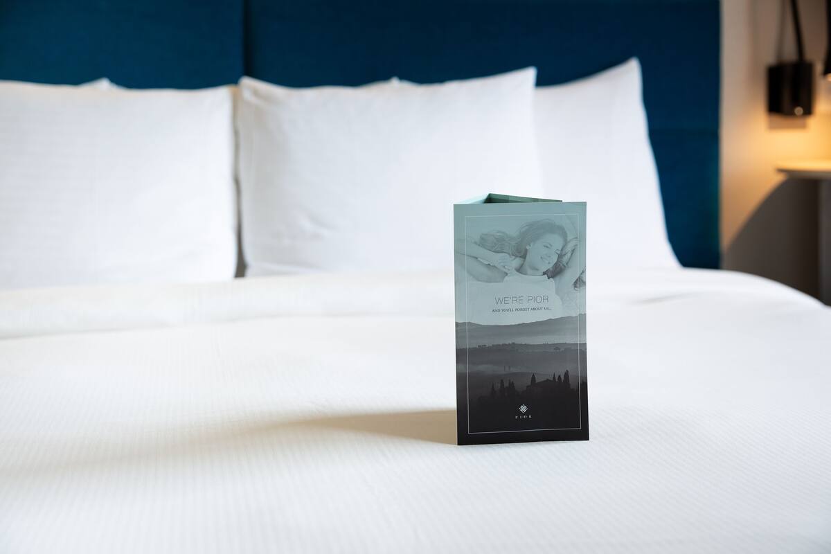 Una cama bien hecha con sábanas blancas y una almohada. Hay un folleto sobre la cama.
