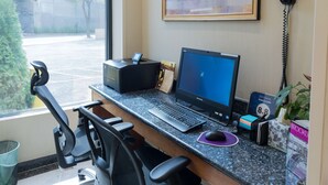 A hotel workspace with a desktop computer, a printer, a laptop, a desk chair, a trash bin, and a framed award on the wall. - Hotel Le Jolie (Brooklyn)