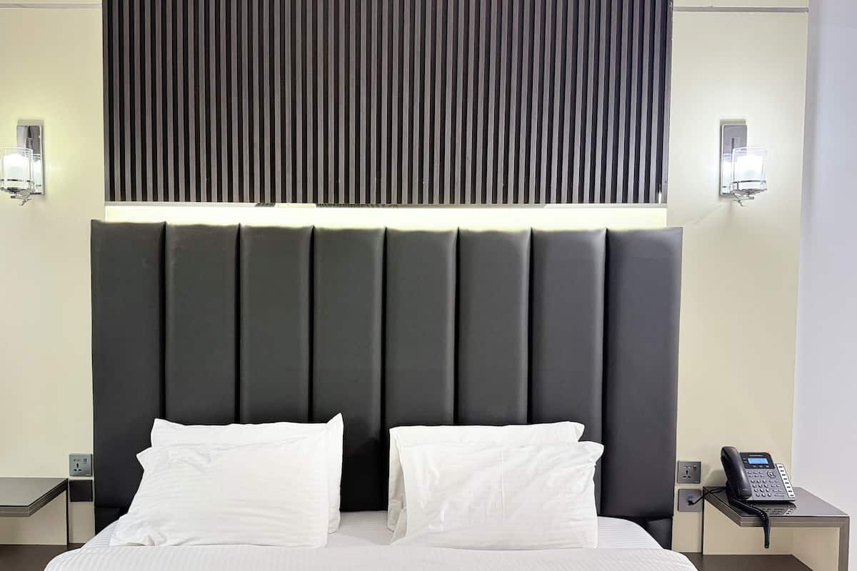 A hotel room with a large bed, two bedside tables, a phone, and a wall-mounted light fixture.