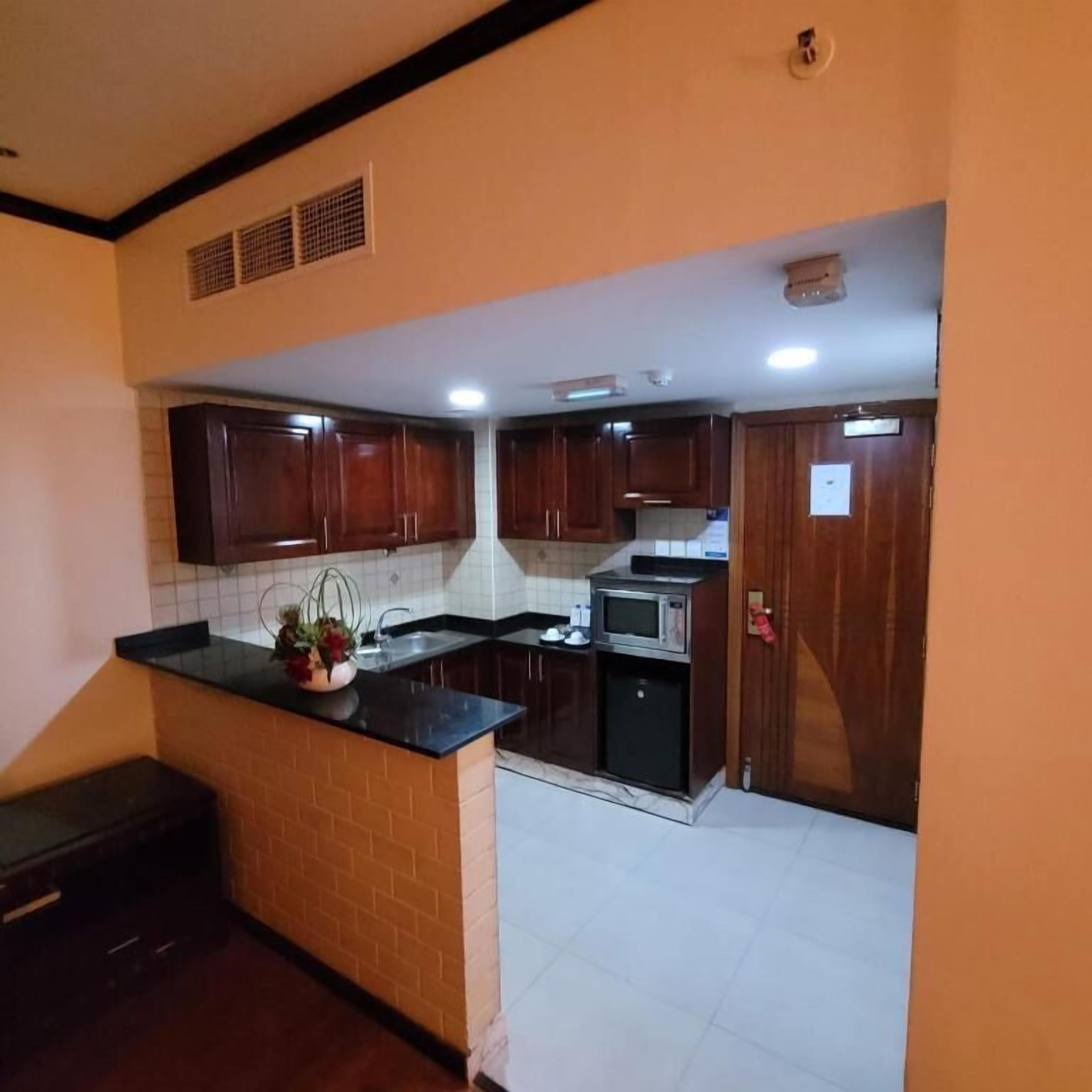 A kitchen with dark wooden cabinets, a black countertop, a microwave, and a sink.