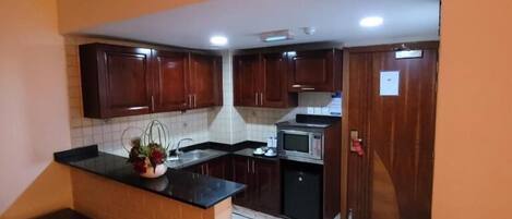 A kitchen with dark wooden cabinets, a black countertop, a microwave, and a sink.