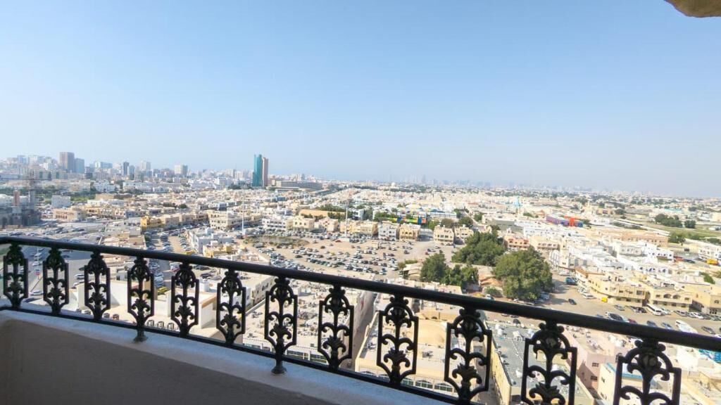A cityscape with a view of buildings and a parking lot from a balcony with ornate railings.