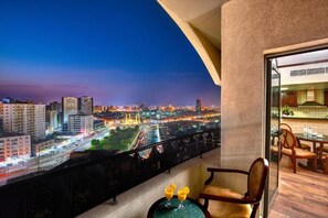 A balcony with a city view at dusk, a dining area with chairs and a table, and two drinks on a small table. - Palette Sharjah Aparthotel formerly Royal Tulip (Sharjah)