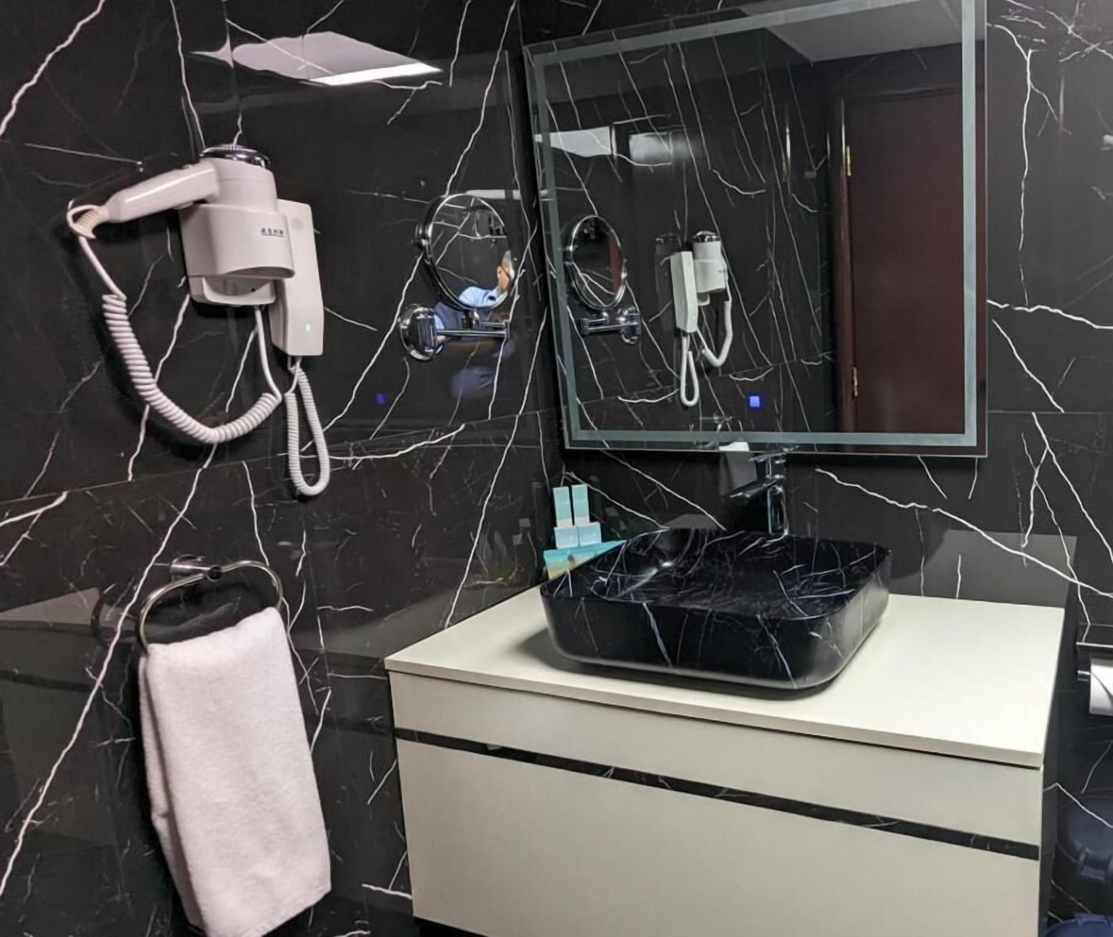 Ein Badezimmer mit einem schwarzen Marmorwaschbecken, einer weißen Kommode, einem Fön und einem Spiegel.
