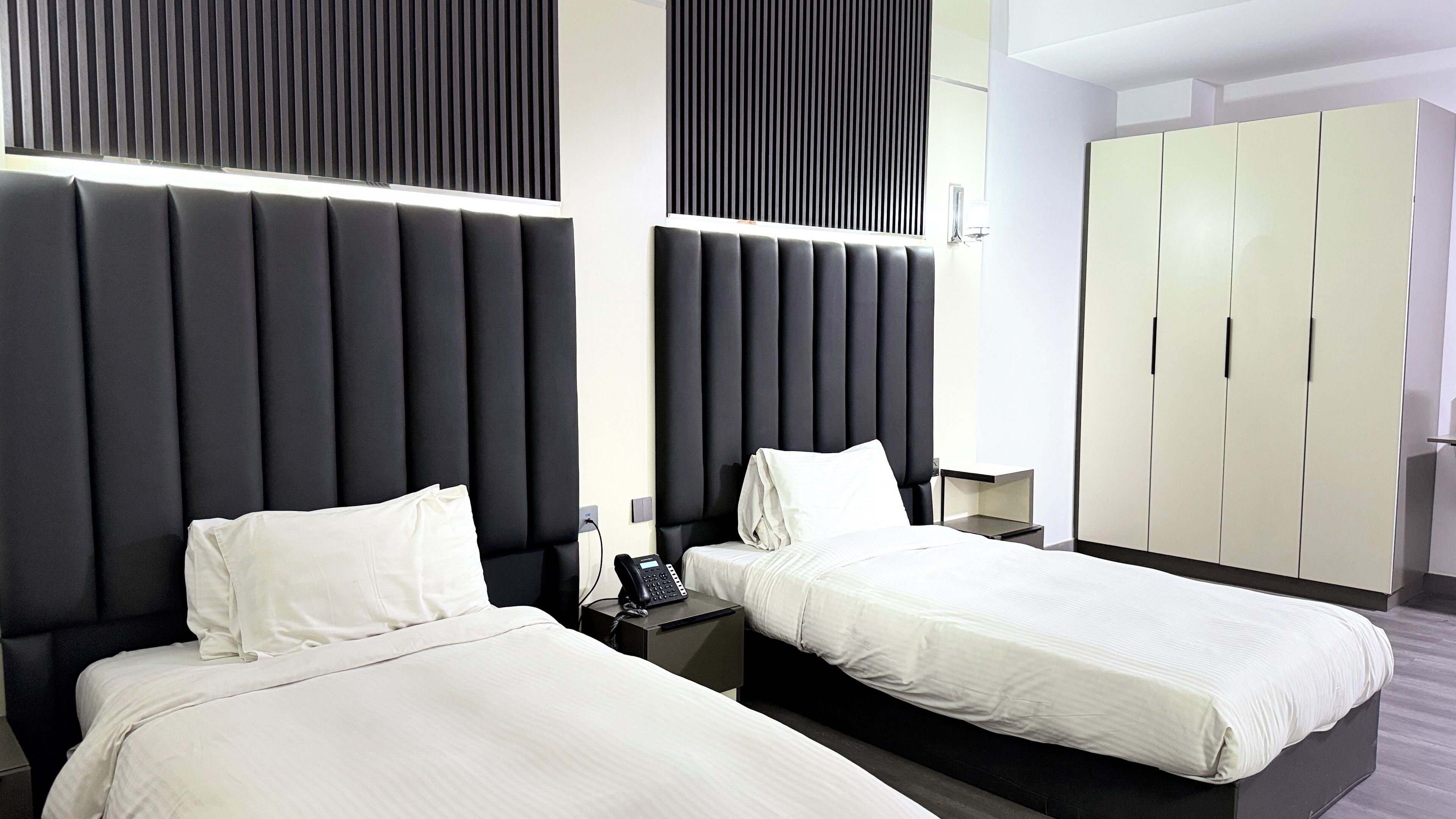 Ein modernes Hotelzimmer mit zwei Betten, einem großen Kleiderschrank und einem Nachttischtelefon.