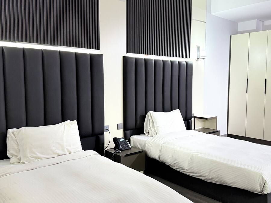 A modern hotel room with two beds, a large wardrobe, and a bedside telephone.