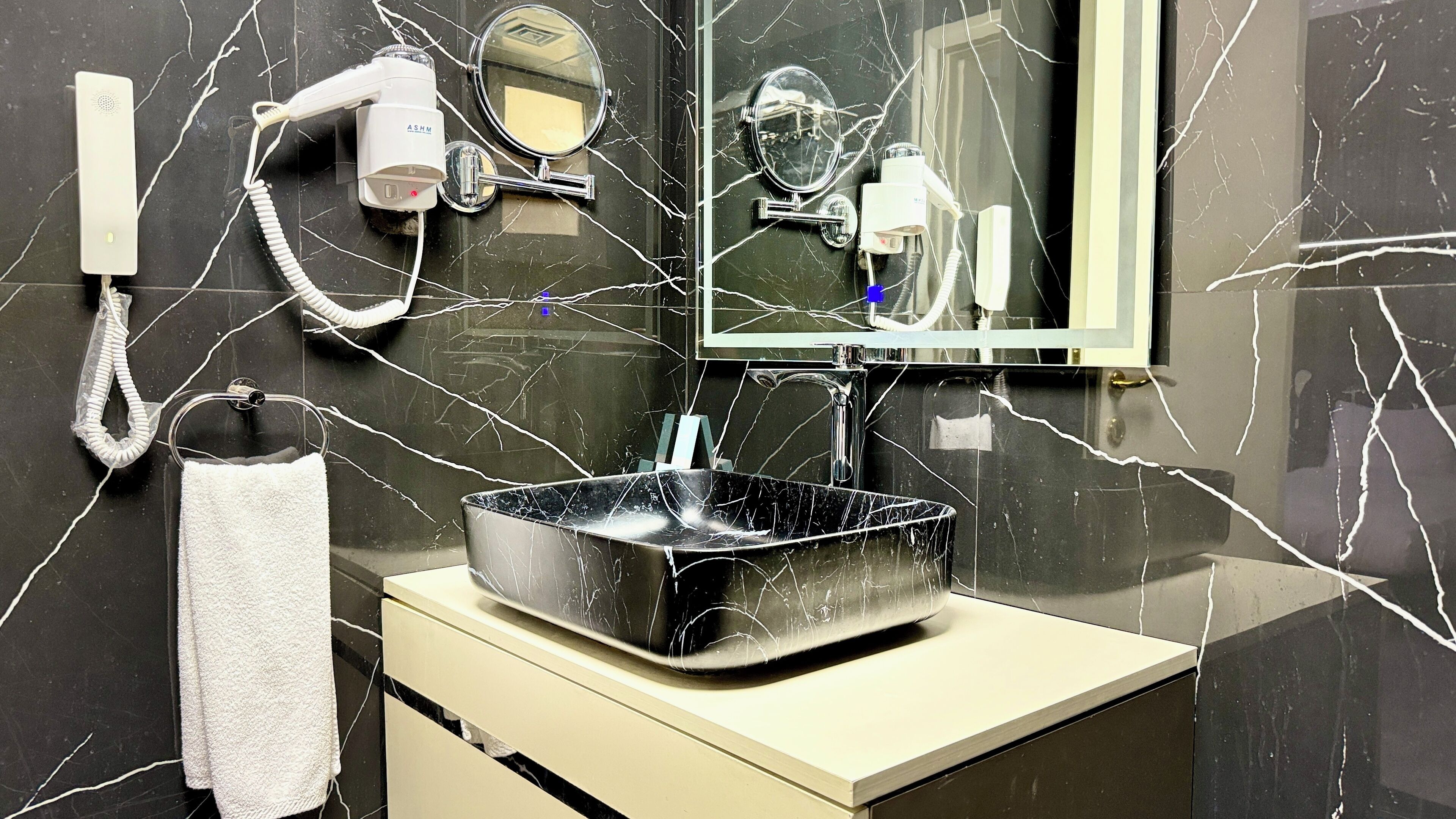 Un bagno con un lavandino in marmo nero, uno specchio e un asciugacapelli montato a parete.