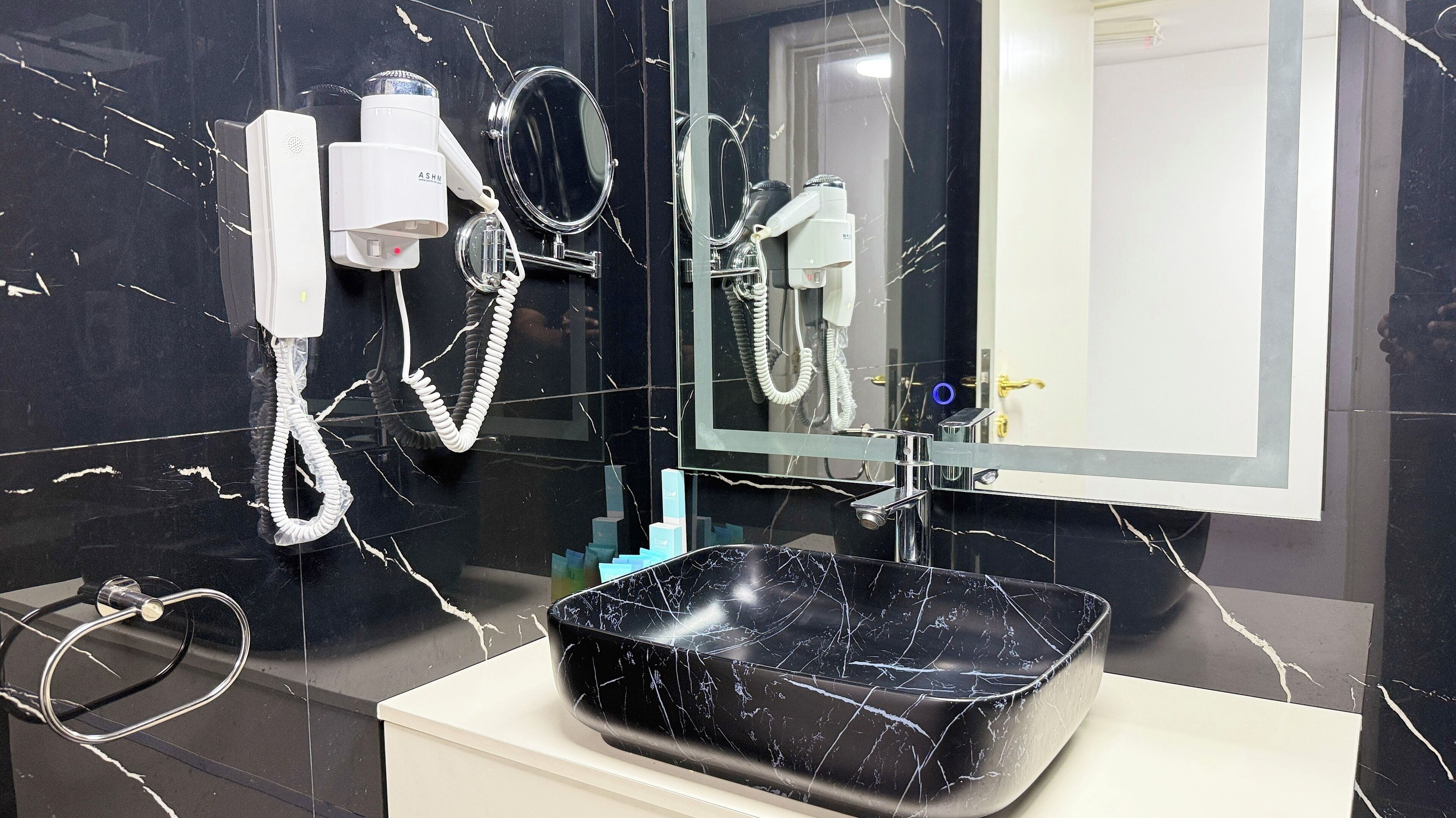 A bathroom with a black marble sink, a white pedestal, a mirror, and a hairdryer.