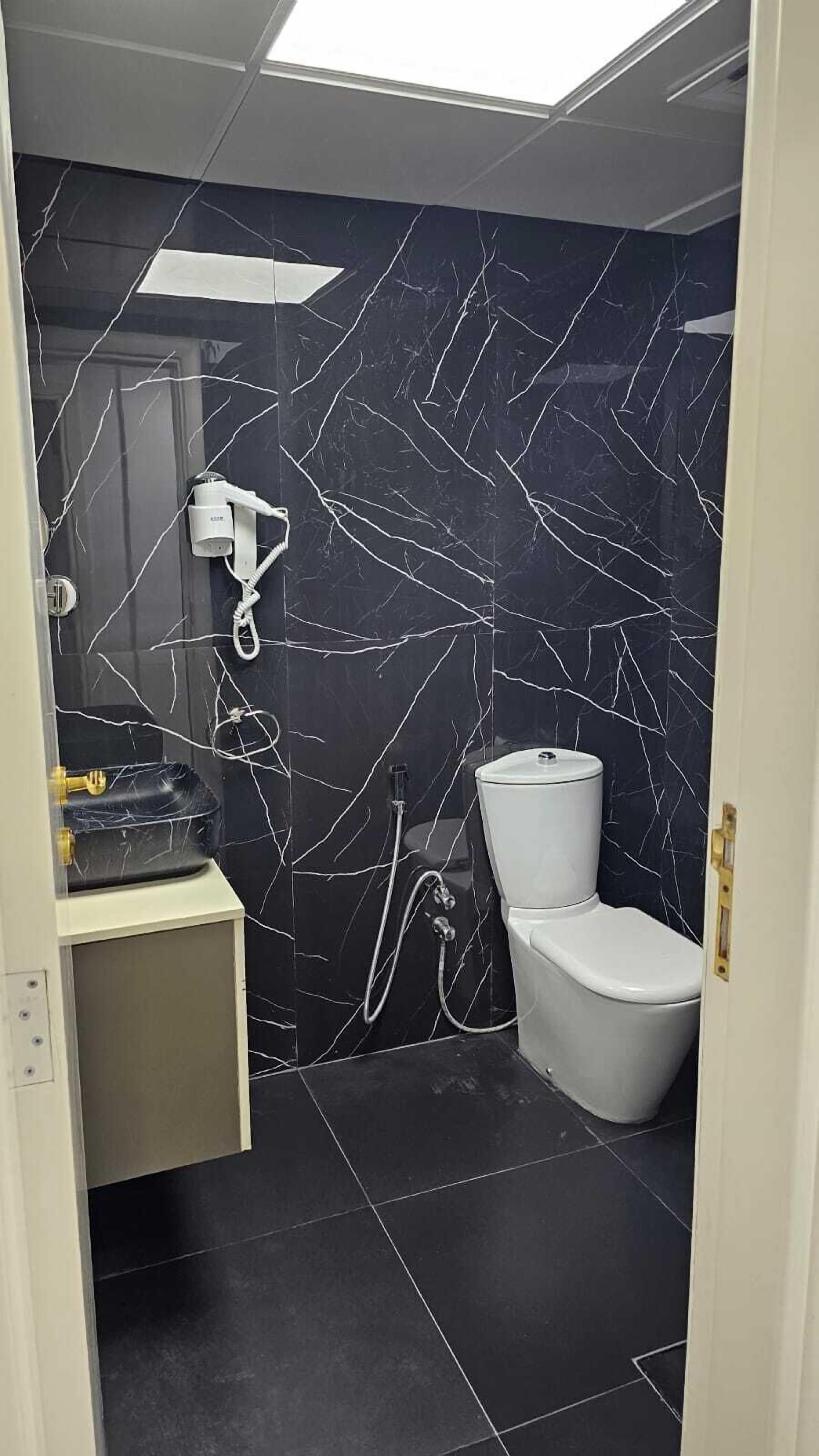 Un baño con pared de mármol negro, inodoro blanco y lavamanos con espejo.